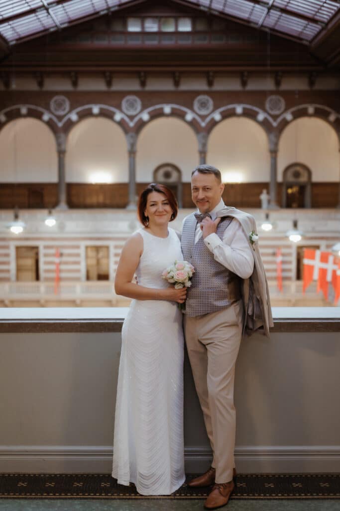 Heiraten in Dänemark: Ein elegantes Brautpaar posiert nach der standesamtlichen Trauung in einem historischen Gebäude mit dänischen Flaggen.