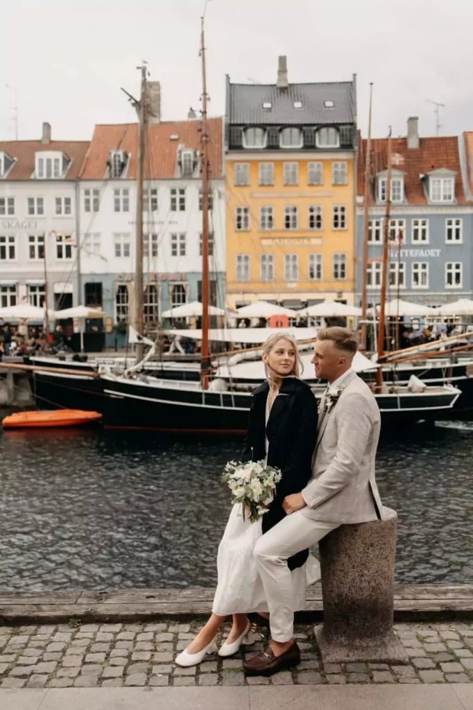 Hochzeitspaar in Nyhavn, Kopenhagen, vor farbenfrohen Häusern und Segelbooten am Wasser.