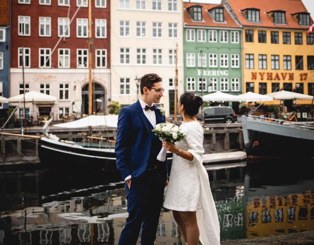 Hochzeitspaar in Nyhavn, Kopenhagen, vor bunten Häusern und einem Kanal mit Segelbooten.