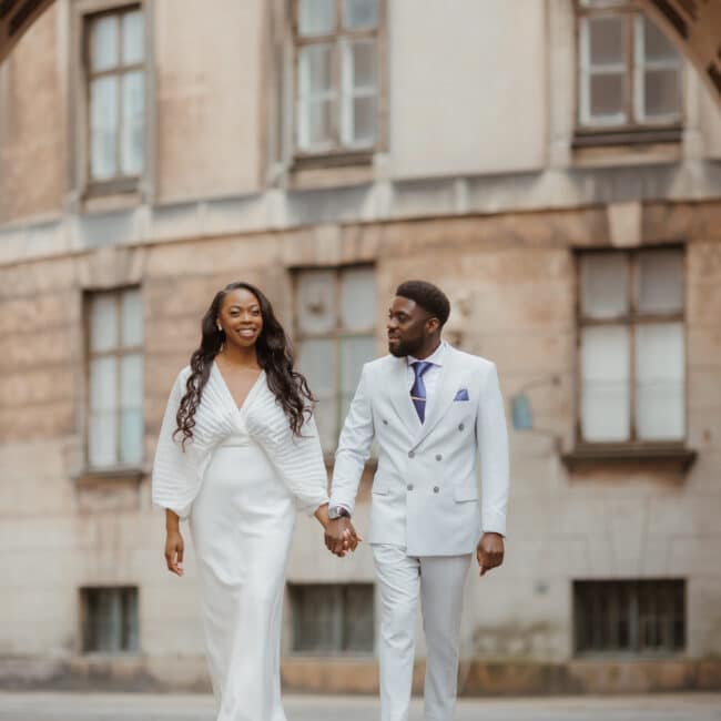 Heiraten in Dänemark: Ein glückliches Brautpaar in eleganter Kleidung spaziert Hand in Hand durch historische Straßen in Dänemark.