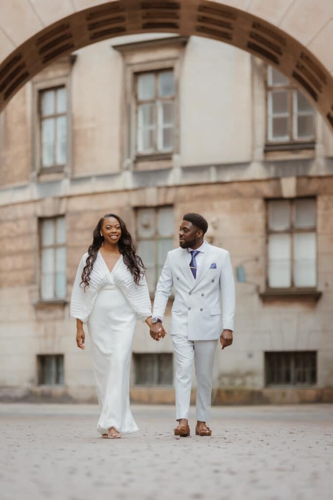 Heiraten in Dänemark: Ein glückliches Brautpaar in eleganter Kleidung spaziert Hand in Hand durch historische Straßen in Dänemark.